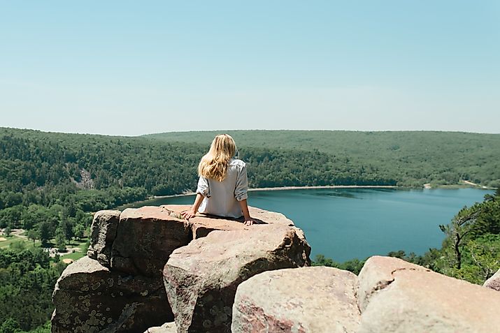 Editorial Photo Credit: Cavan-Images via Shutterstock. High angle of female sitting on cliff at Devil's Lake State Park, WI