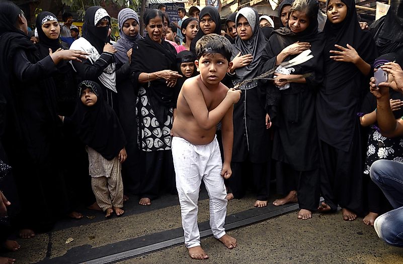 A criança xiita se flagela com Zanzir, enquanto as mulheres muçulmanas o observam na ocasião da procissão do Muharram.  Crédito da imagem: Saikat Paul / Shutterstock.com