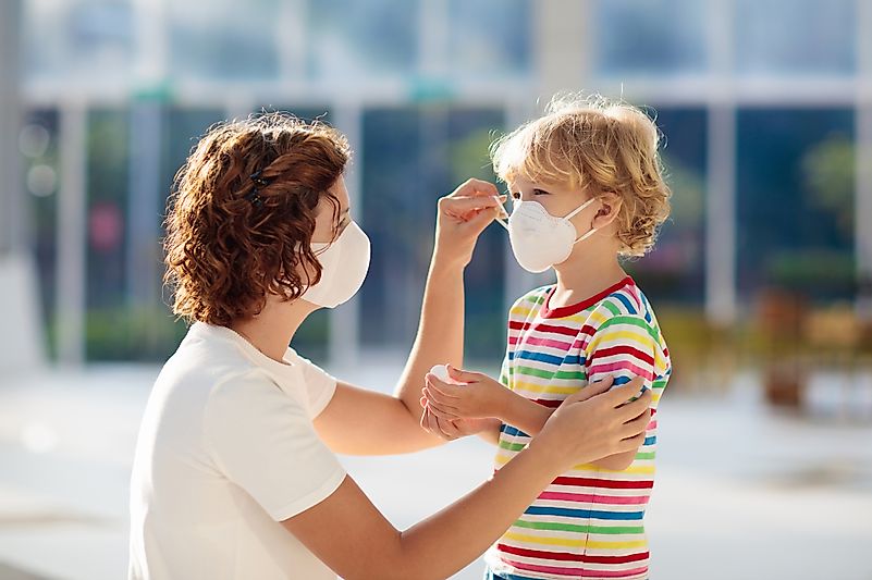 A mother helps her son put on a face mask as a precaution to combat the COVID-19. Image credit: FamVeld/Shutterstock.com
