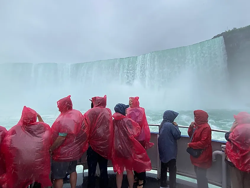 A boat full of red poncho wearing passengers approaches the massive misty curve of Horseshoe Falls.