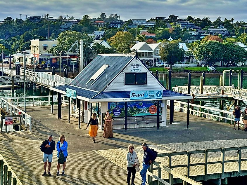 Tourists walking along Russell Wharf with the Russell Radio building and waterfront shops in the Bay of Islands, New Zealand.