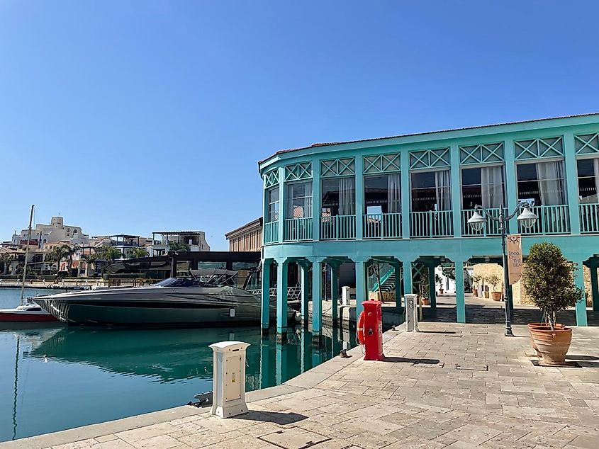 A sea foam blue Venetian building stands beside a yacht in a Mediterranean marina.