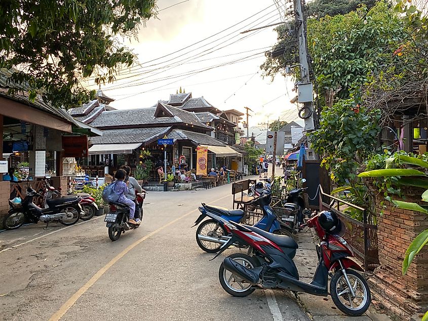 A mother and daughter on a motorcycle ride off onto a slim, paved street in Thailand.