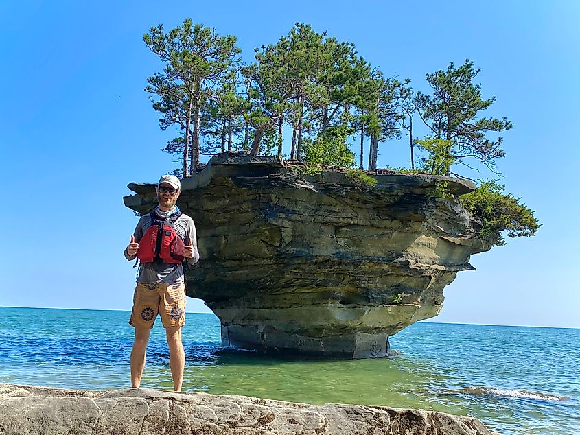 The author stands on a rocky shore in front of the enigmatic floating island known as Turnip Rock.