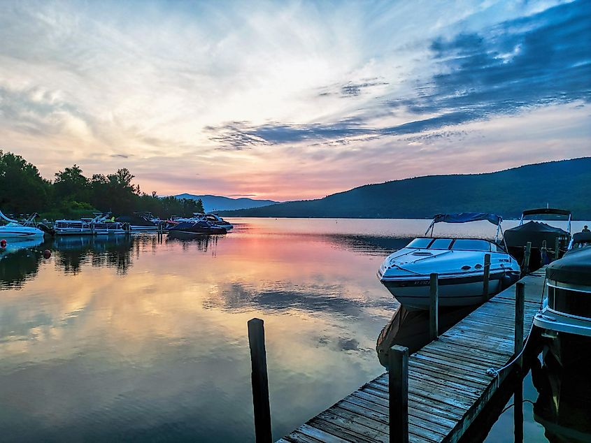 Sunrise over Lake George, New York, with boats moored near the shore and a deck in the scene.
