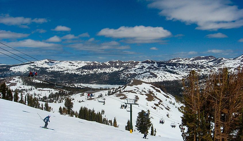 A skier works his way down the slope on a bright, sunny day with blue skies.