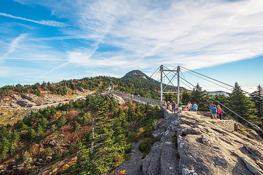 People are hiking on Grandfather mountain trail with view of Mile High Swinging Bridge on background in Grandfather mountain state park.