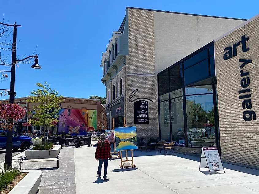 A man in a red plaid walks past a small town art gallery, toward a colorful mural on the next building