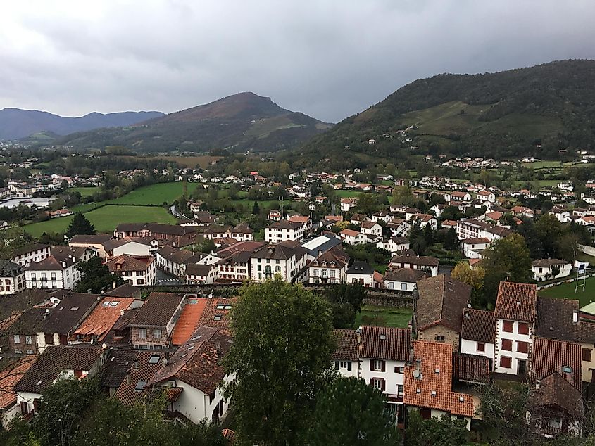 A high-angle view of a small French mountain village. Rustic red roofs are scattered beneath a gloomy sky.  