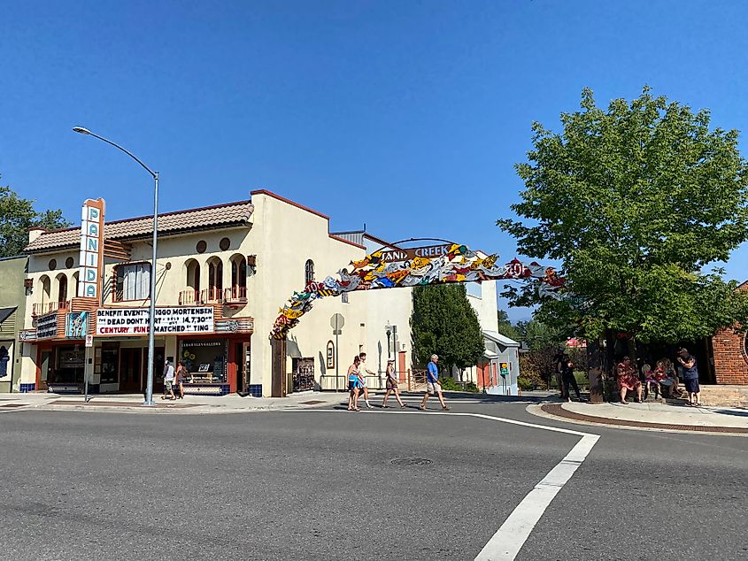 A family crosses a chill street with a marquee movie theatre on it. 