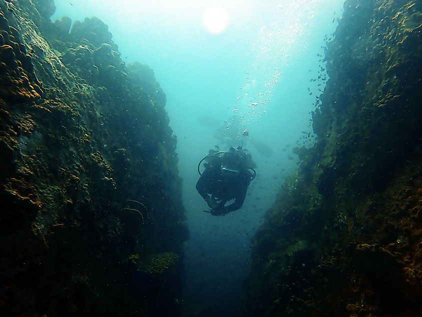 Diver swimming through a narrow rock gaps in the sea.