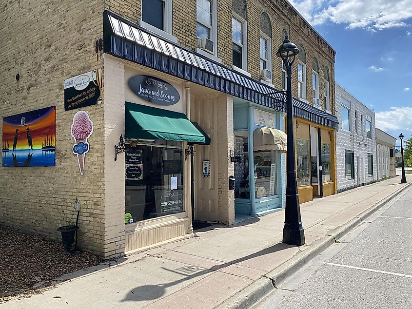 A block of small-town shops with uniquely coloured storefronts and a bright mural on the red brick side wall