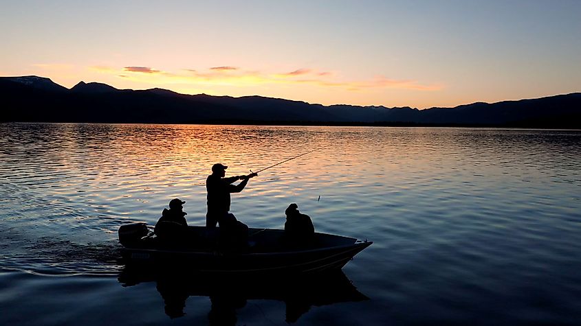 People fishing in a boat floating on Hebgen Lake during colorful sunset