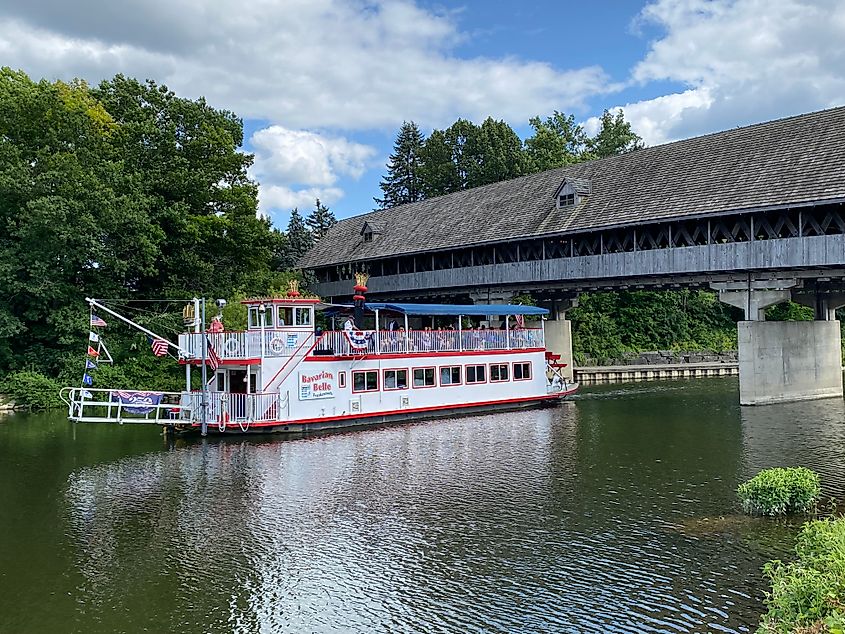 A traditional paddlewheel boat passes underneath a wooden covered bridge. 