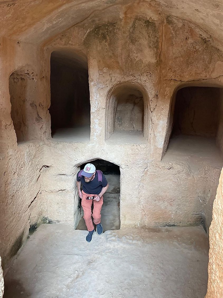 A man with a ball cap and a backpack emerges from a cavern within a subterranean ruin