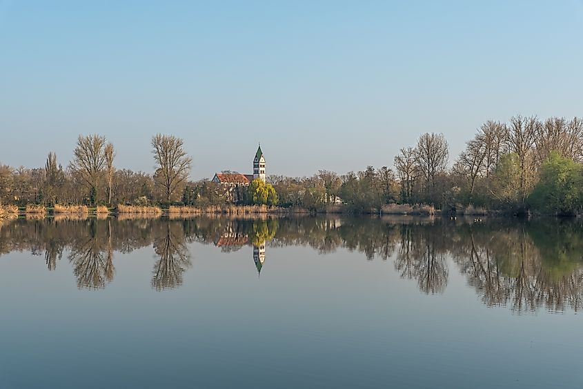 Fishing lake and St. Sebastian Church in morning light, Ketsch, Baden-Wuerttemberg, Germany