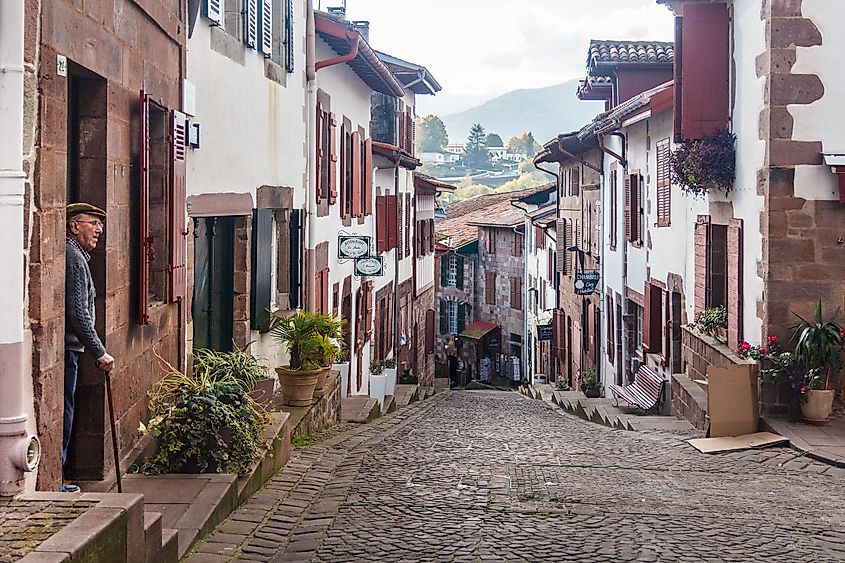 An old man looks out from his home onto an old-fashioned French cobblestone street