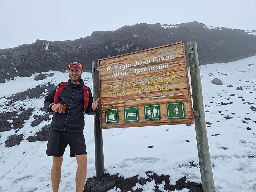 A runner standing next to the altitude sign on a snowy volcano