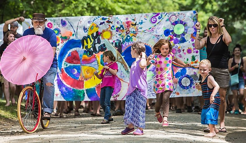 Excited children adults walking down road with colorful banner and umbrella at the Wild Goose Festival in Hot Springs, North Carolina.