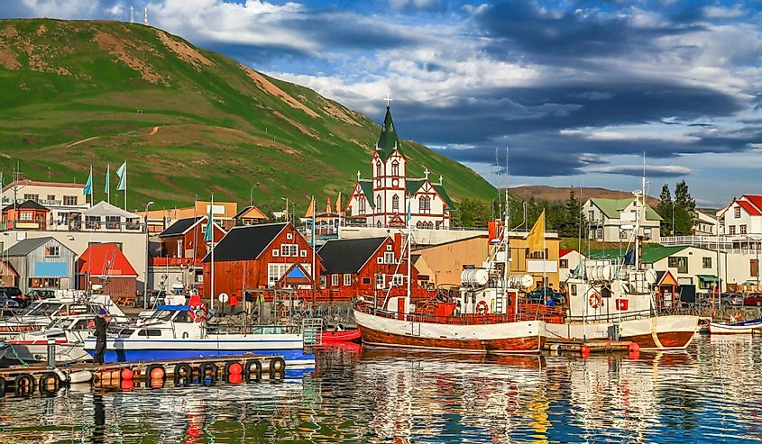 Beautiful view of the historic town of Husavik with traditional colorful houses and traditional fisherman boats lying in the harbor in golden evening light at sunset, northern coast of Iceland