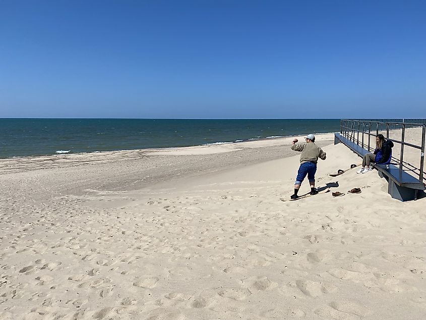 A couple learning how to sandboard on a small dune beside Lake Michigan