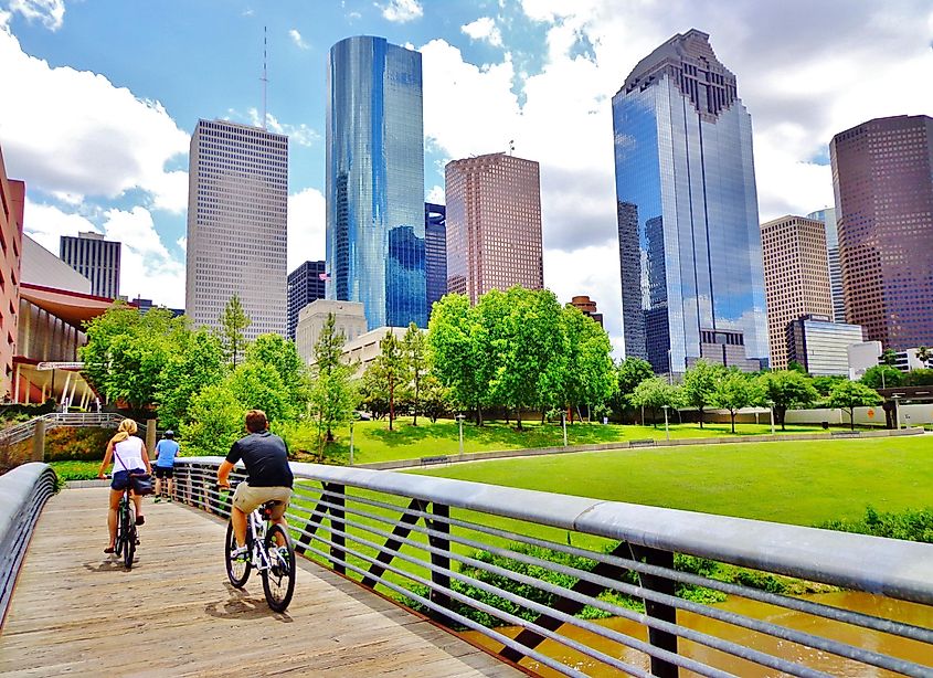 Bicyclists cross wooden bridge in Buffalo Bayou Park, with a beautiful view of downtown Housto