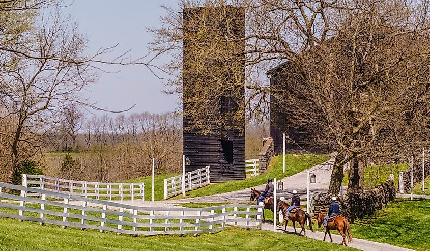 Three adult riders follow a trail toward an historic barn at the landmark destination of Shaker Village of Pleasant Hill on a sunny day in spring, Harrodsburg.