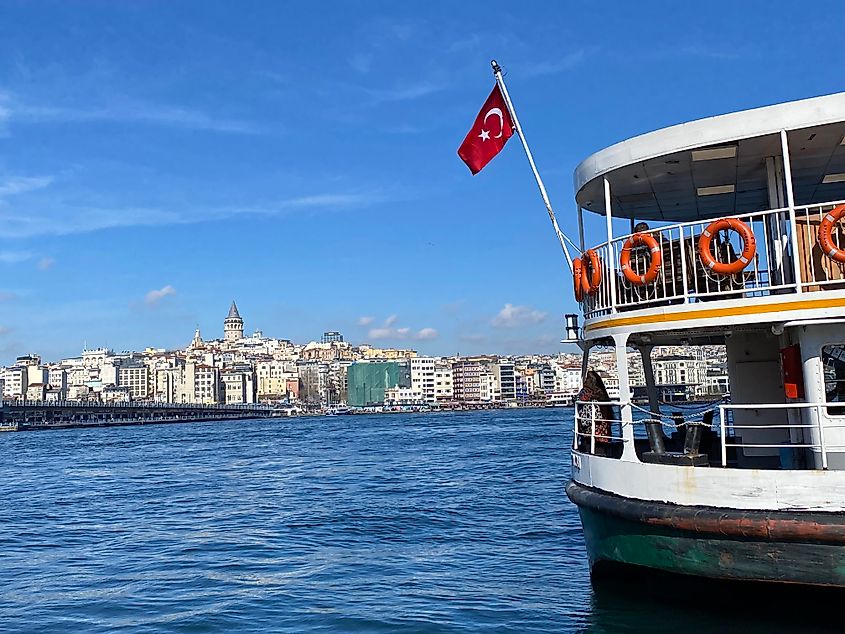 A river ferry baring Turkey's red flag anchored across from a dense neighborhood in Istanbul.