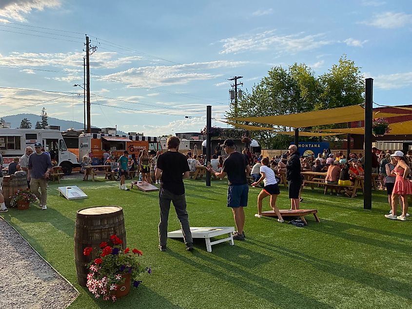 People play beanbag in a park lined with food trucks and stacked with picnic tables