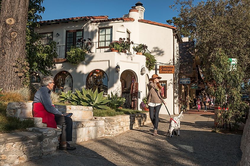 A fashionably-dressed tall woman strolls down a sidewalk along with her dog at Carmel-By-The-Sea, California