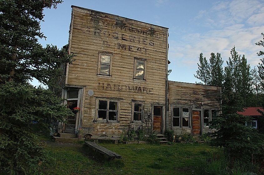 The McCarthy hardware store in decrepit condition surrounded by trees against a blue sky.