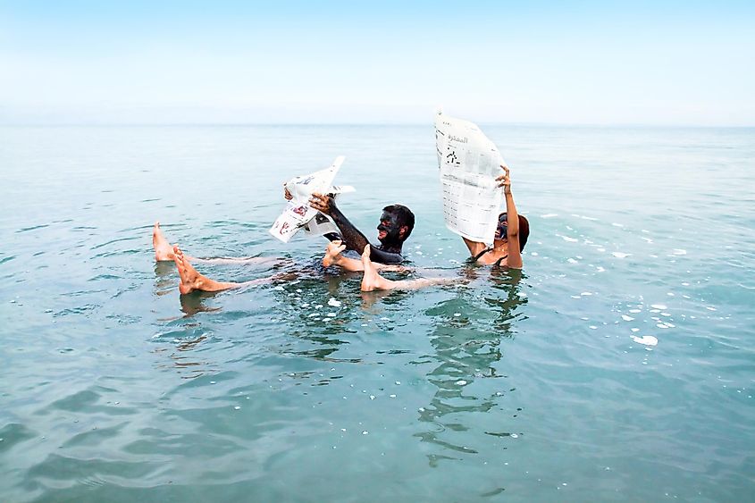 People with mud masks floating in the Dead Sea while reading newspapers.