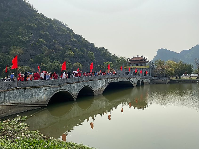 A stone bridge lined with red flags leads to a large stone gate of an ancient Vietnamese city.
