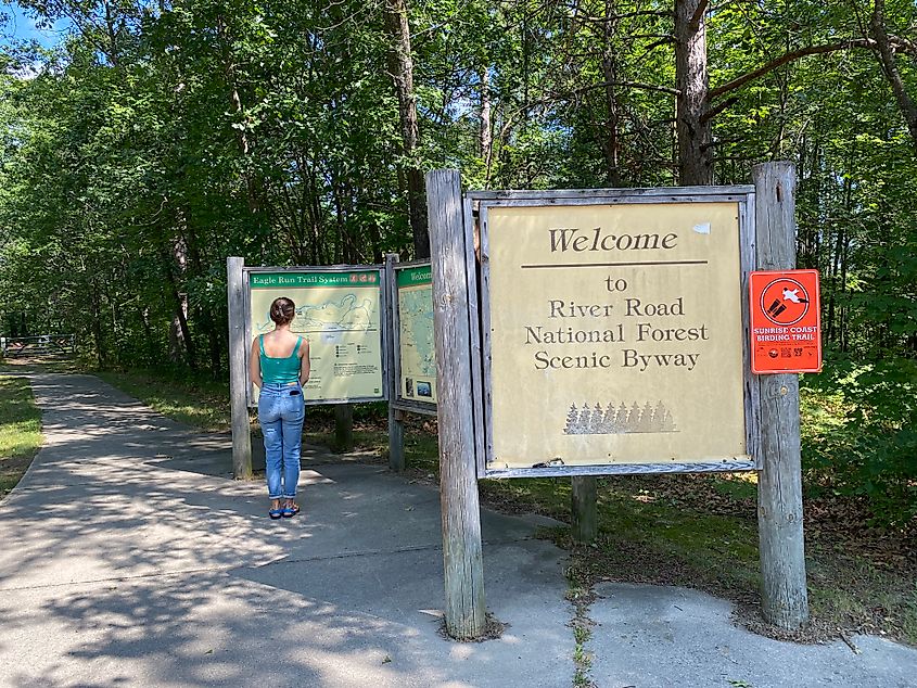 A woman in jeans and green tank top reads the signs for the River Road National Scenic Byway.