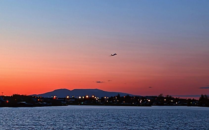 View of the Lake Hood Seaplane Base at sunset, with a plane flying over Lake Hood. 