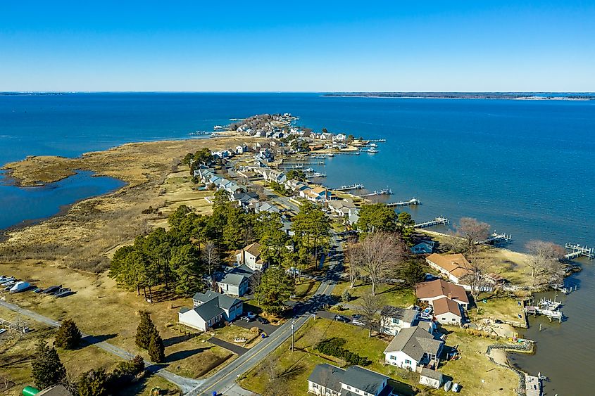 Aerial view of Kent Narrows peninsula inlet on Chesapeake in Grasonville Maryland, beach houses with private long docks for the sailboats line a road curving like an S shape with blue sky and water