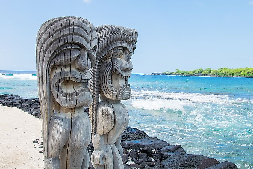 Carved Polynesian figures standing on a Pacific shoreline