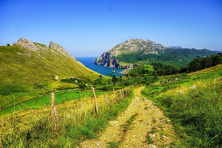 A dirt road follows the edge of rugged green mountains and the coast of the Atlantic Ocean.