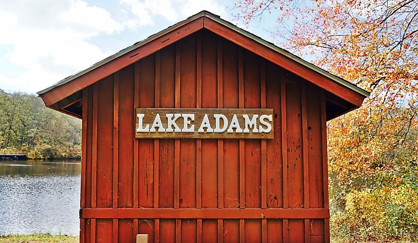 A horizontal image of a red wooden boat house overlooking a freshwater pond.