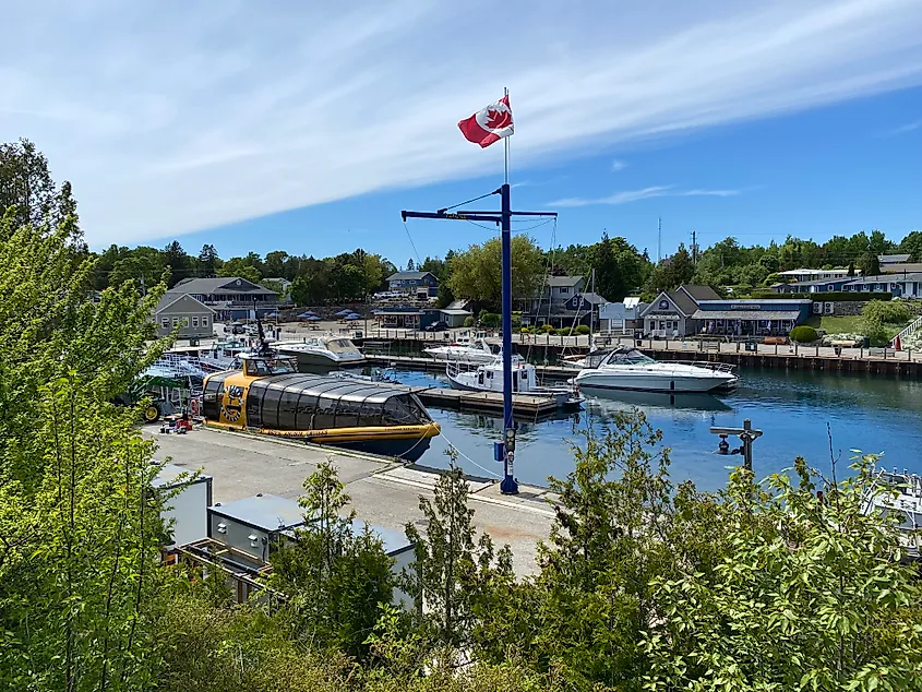 A Canadian flag stands at the heart of a small, idyllic harbour, as seen through the trees.