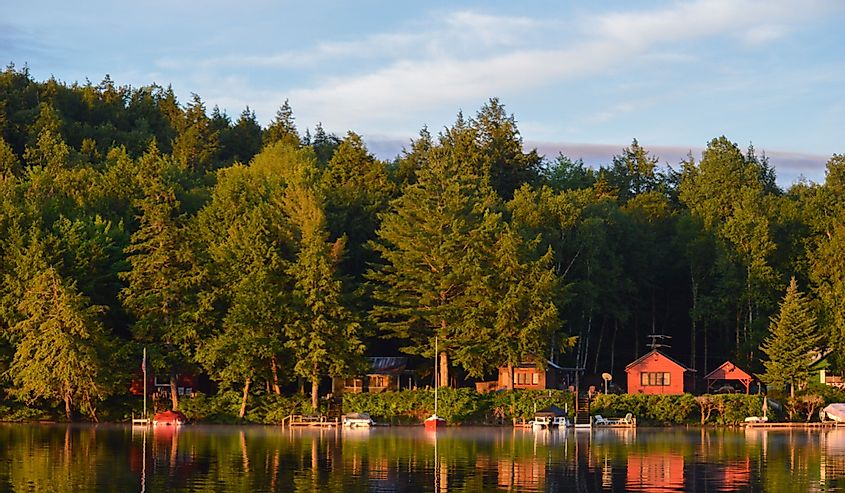 Cabin coastline on Saranac Lake in upstate New York bathed in the morning sunrise. The colored cabins are reflected in the water