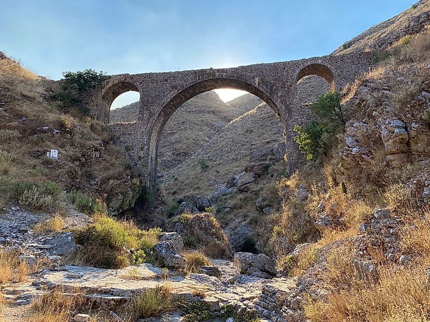 An antiquitous aqueduct blends into the rocky, yellow-grey hills