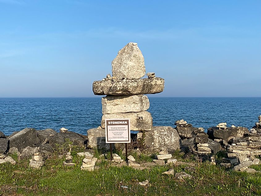 A large stone inukshuk called "Stoneman" stands before a rocky lakeshore.