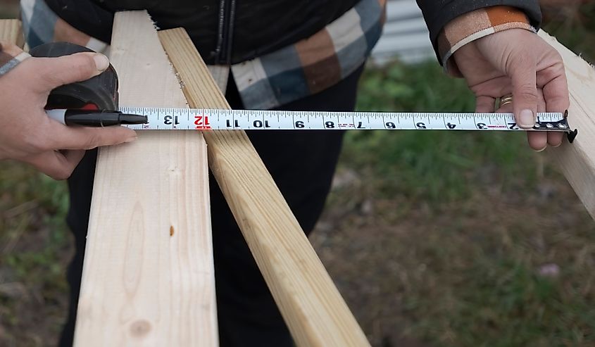Closeup of hands of a female carpenter measuring ONE FOOT (12 inches) on a wood plank.