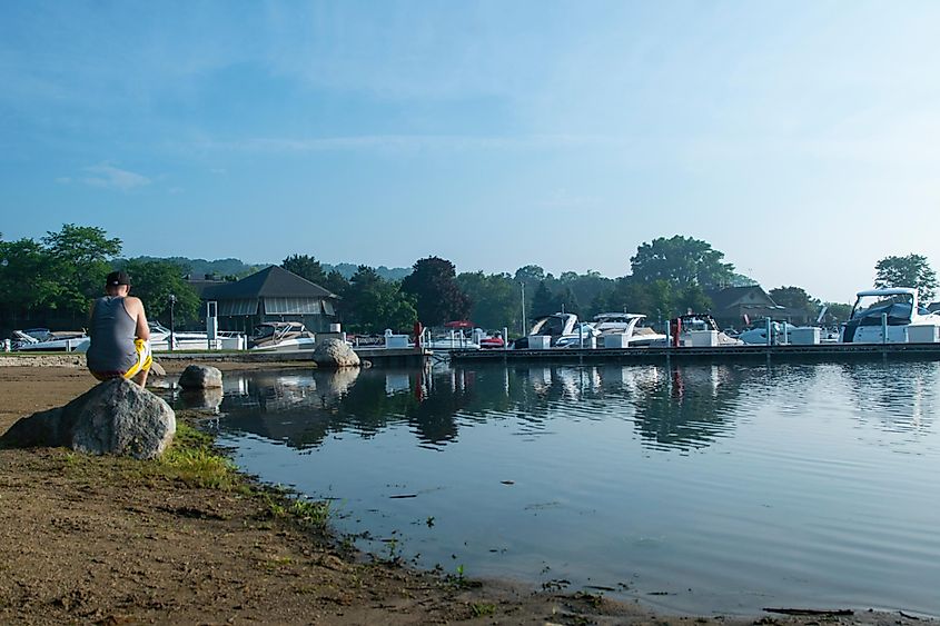 A man sit on a rock near the lake next to luxury boats in Lake Geneva, Wisconsin