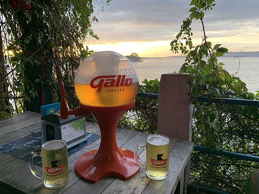 A large bowl of beer and two filled glasses on a patio overlooking the water. 