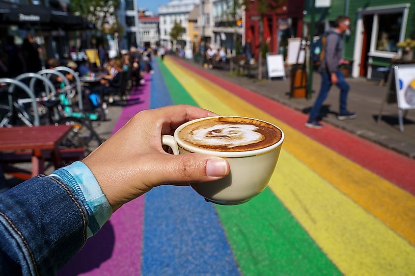 Hand holds up a cappuccino coffee while dining along the famous rainbow street in Reykjavik Iceland