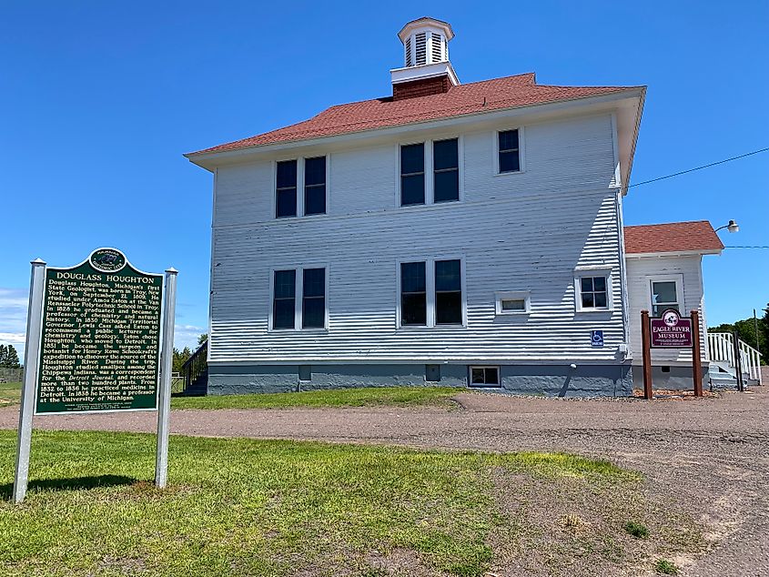 The white panelled exterior of the Eagle River Museum with a green interpretive sign out front.