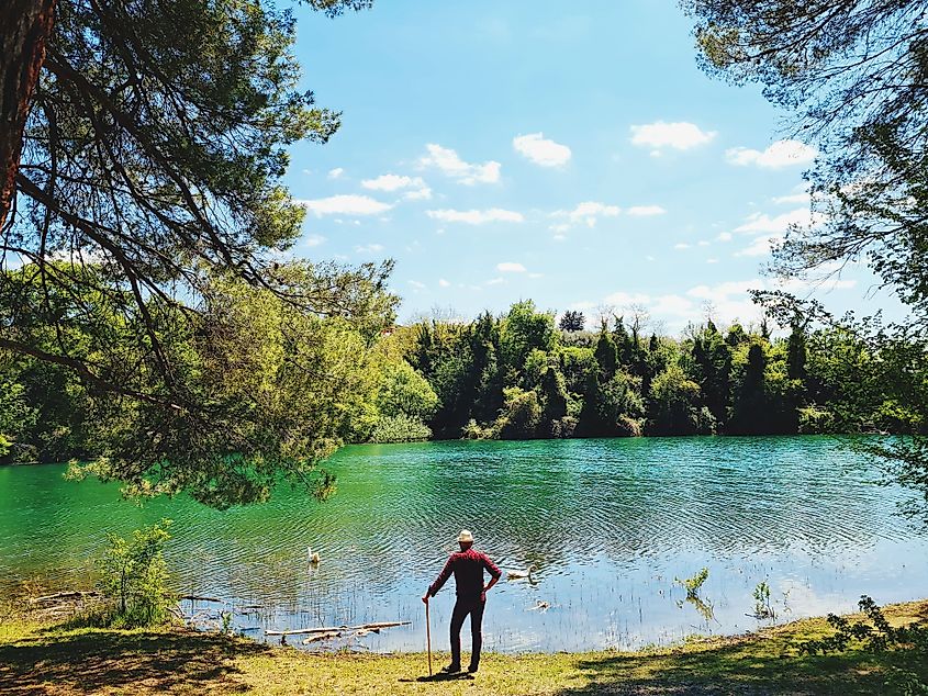 A back view of a hiker with a walking stick observing the beautiful Penne Lake in Abruzzo