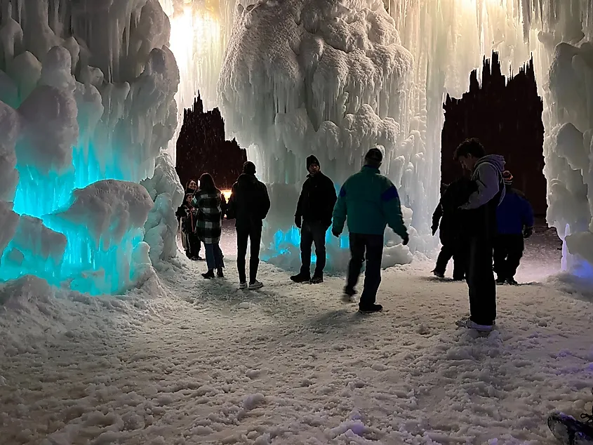 People in winter clothing explore an ice cave with illuminated blue-green walls and icicles, creating a magical, awe-inspiring atmosphere.